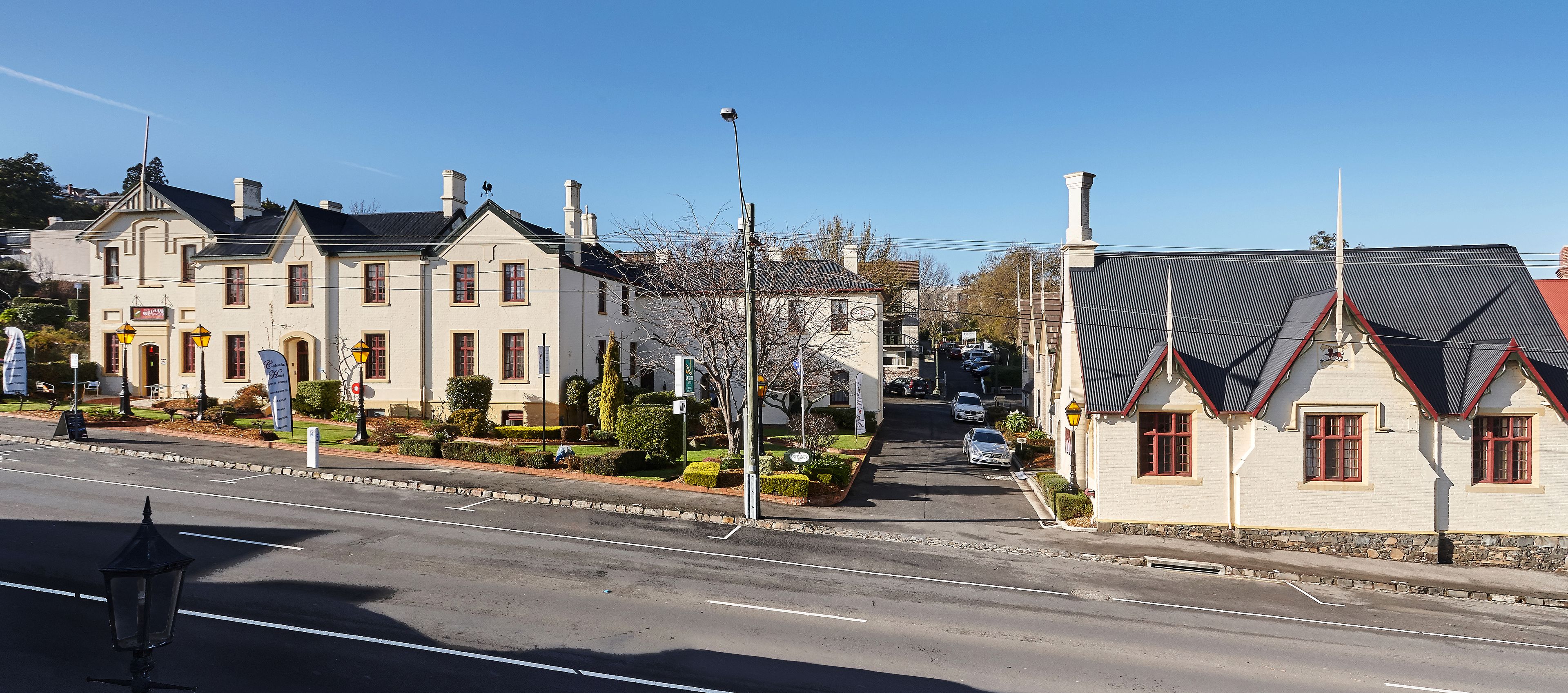 Straßenansicht eines großen, historischen Gebäudes mit mehreren Schornsteinen und eines kleineren, angrenzenden Gebäudes mit rotem Dach.