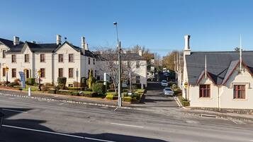 A street view with a large, historic building with multiple chimneys and a smaller adjacent building with a red roof.