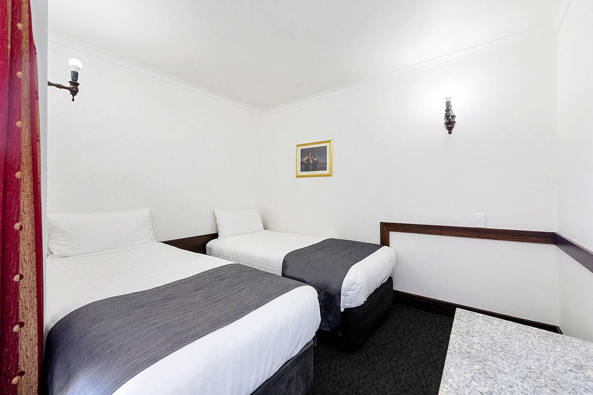 A hotel room with two beds, a small framed picture on the wall, and a red curtain on the left.