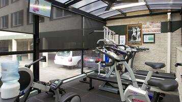 A gym with exercise equipment, a water dispenser, and a view of parked cars outside.