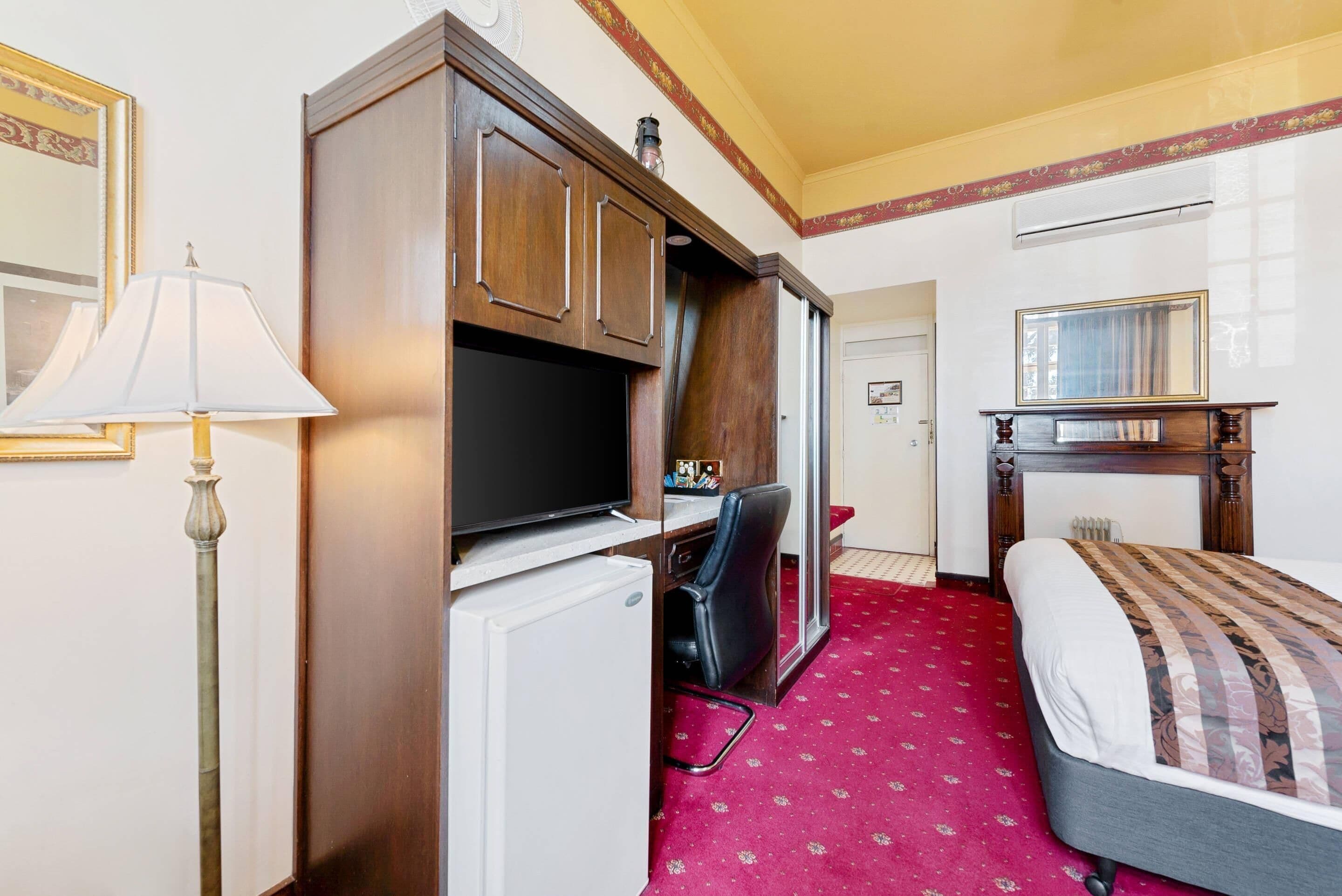 Habitación de hotel con cama, escritorio con computadora, silla, lámpara y televisión.