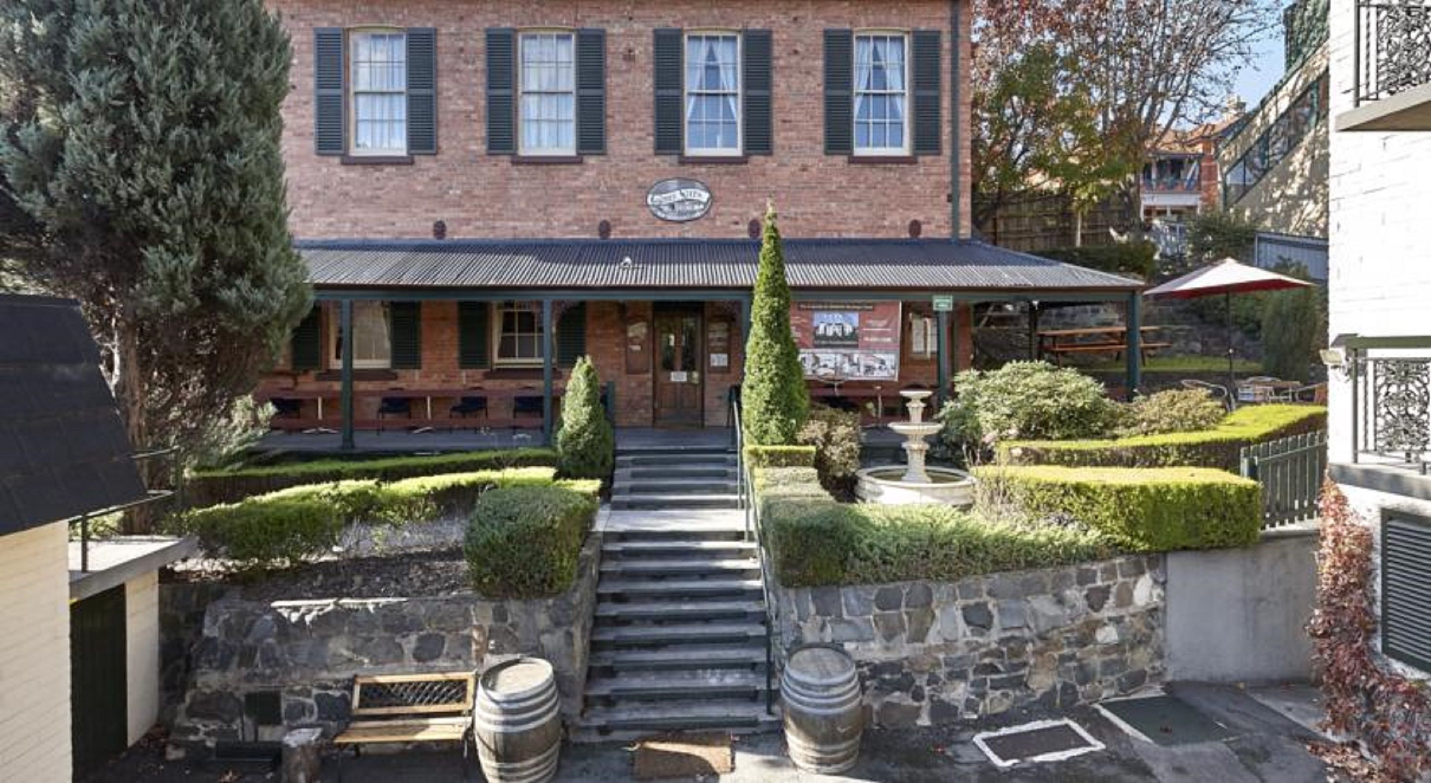A brick building with a covered patio, stone steps, and a small fountain.