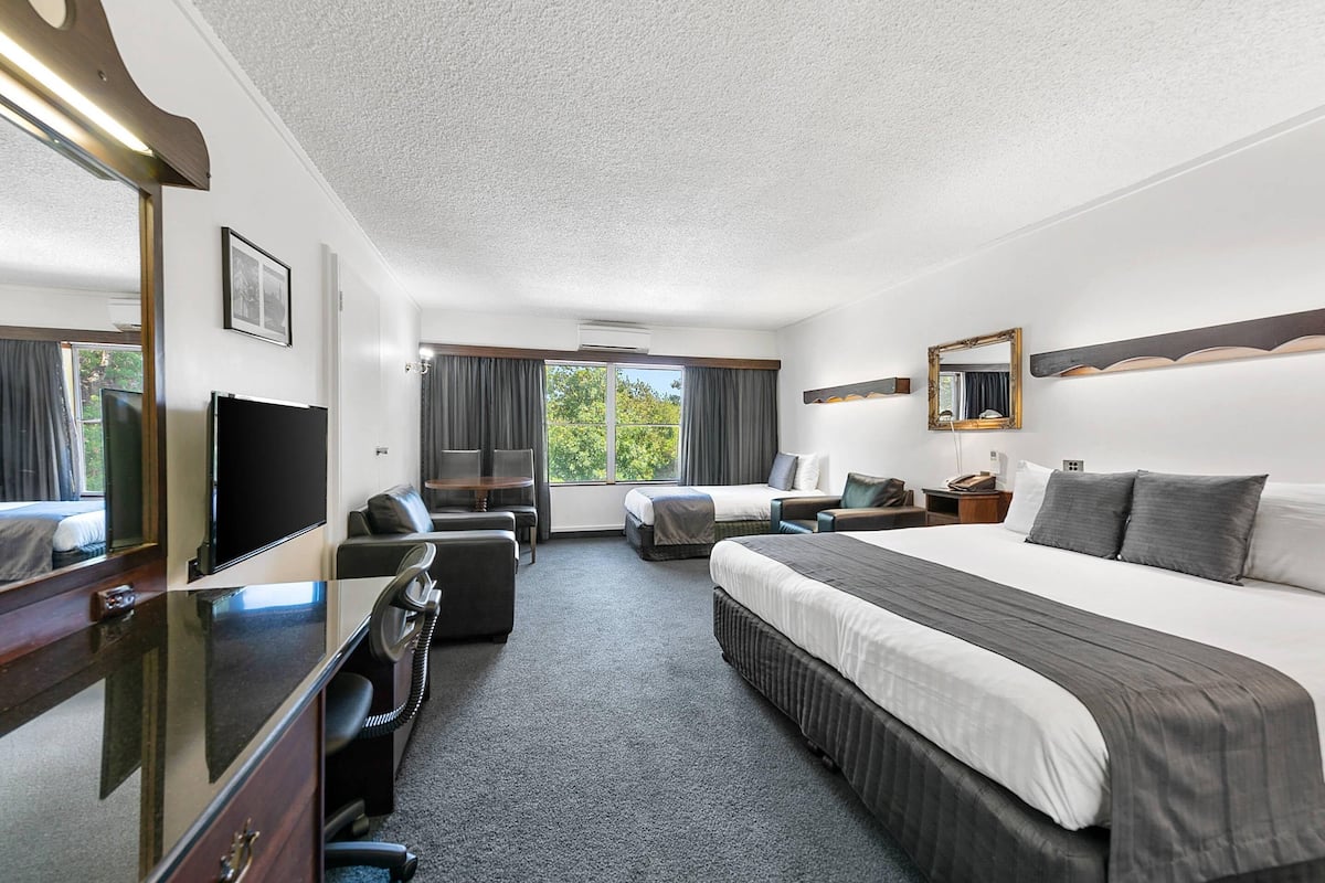 A hotel room with a bed, desk, chair, TV, and a large window with curtains.
