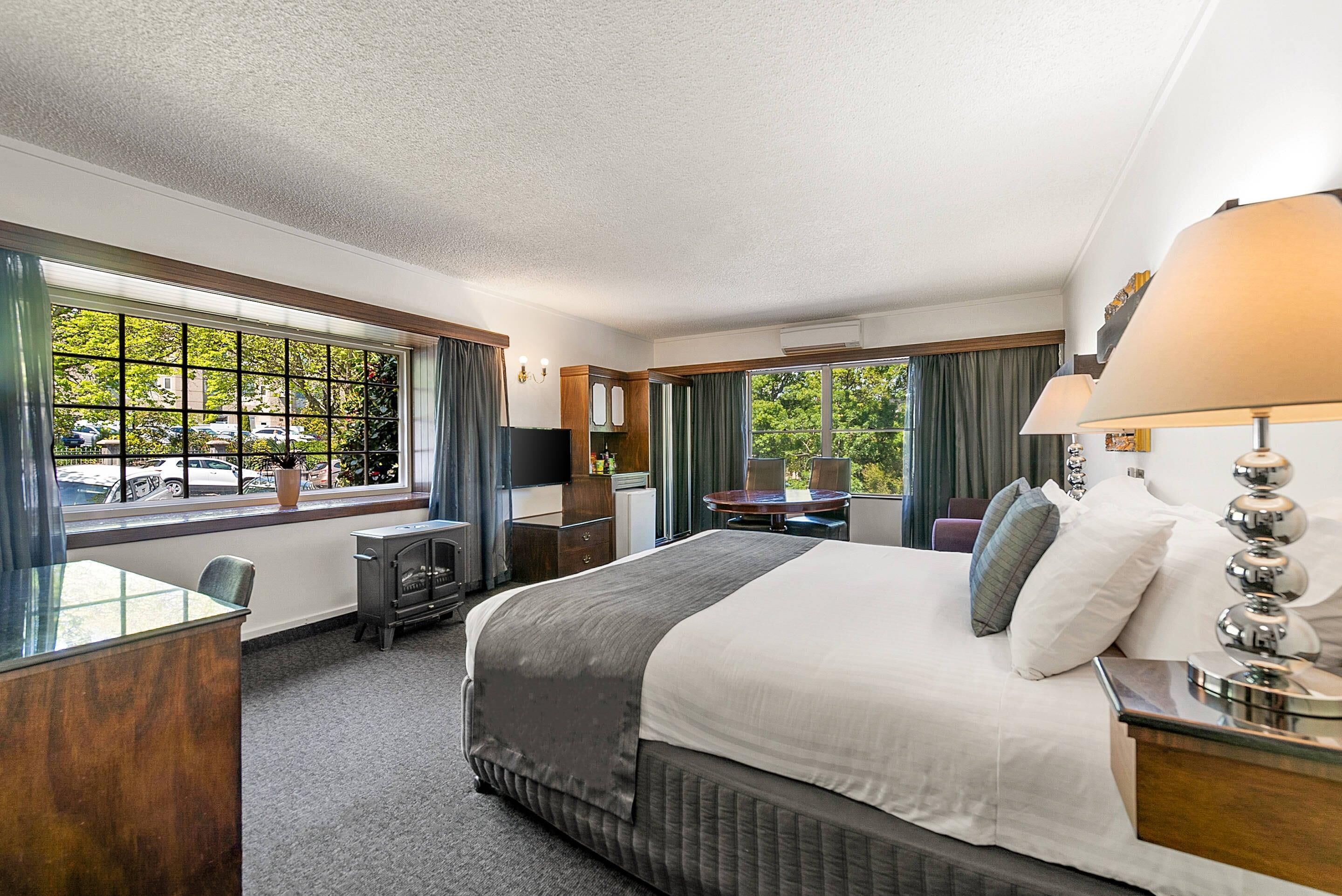 A hotel room with a large bed, a desk, a chair, a TV, and a window with a view of the outside.