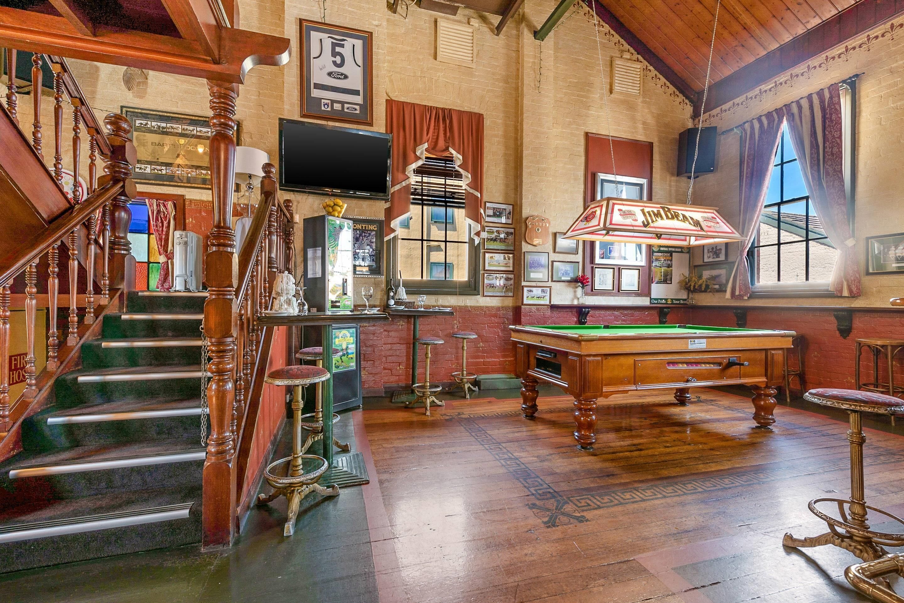 A billiards room with a pool table, a bar area, and a staircase.
