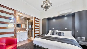 Una habitación de hotel moderna con una cama grande, una silla roja, un separador de vidrio y un candelabro.