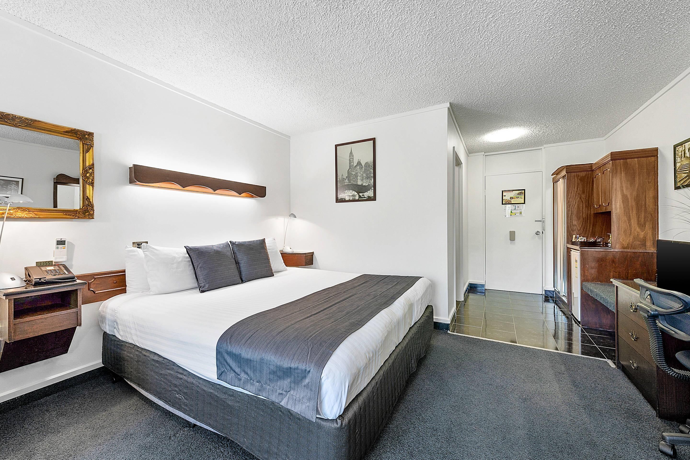 A hotel room with a large bed, bedside tables, a desk, a chair, a wardrobe, and a mirror.