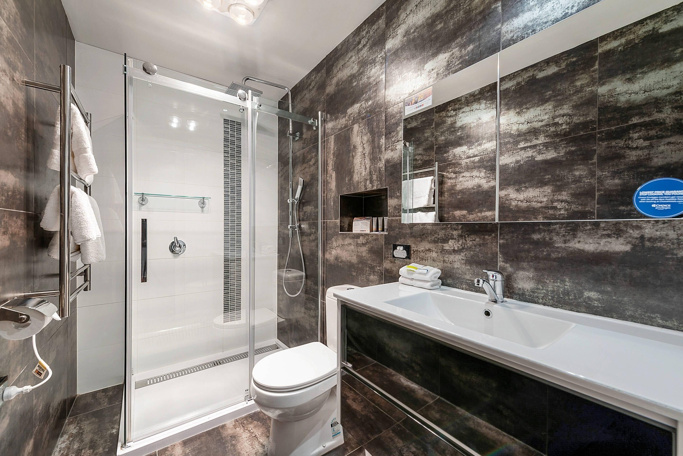 A modern bathroom with a glass-enclosed shower, a white toilet, and a large sink with a mirror above.