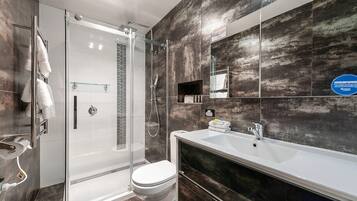 A modern bathroom with a glass-enclosed shower, a white toilet, and a large sink with a mirror above.