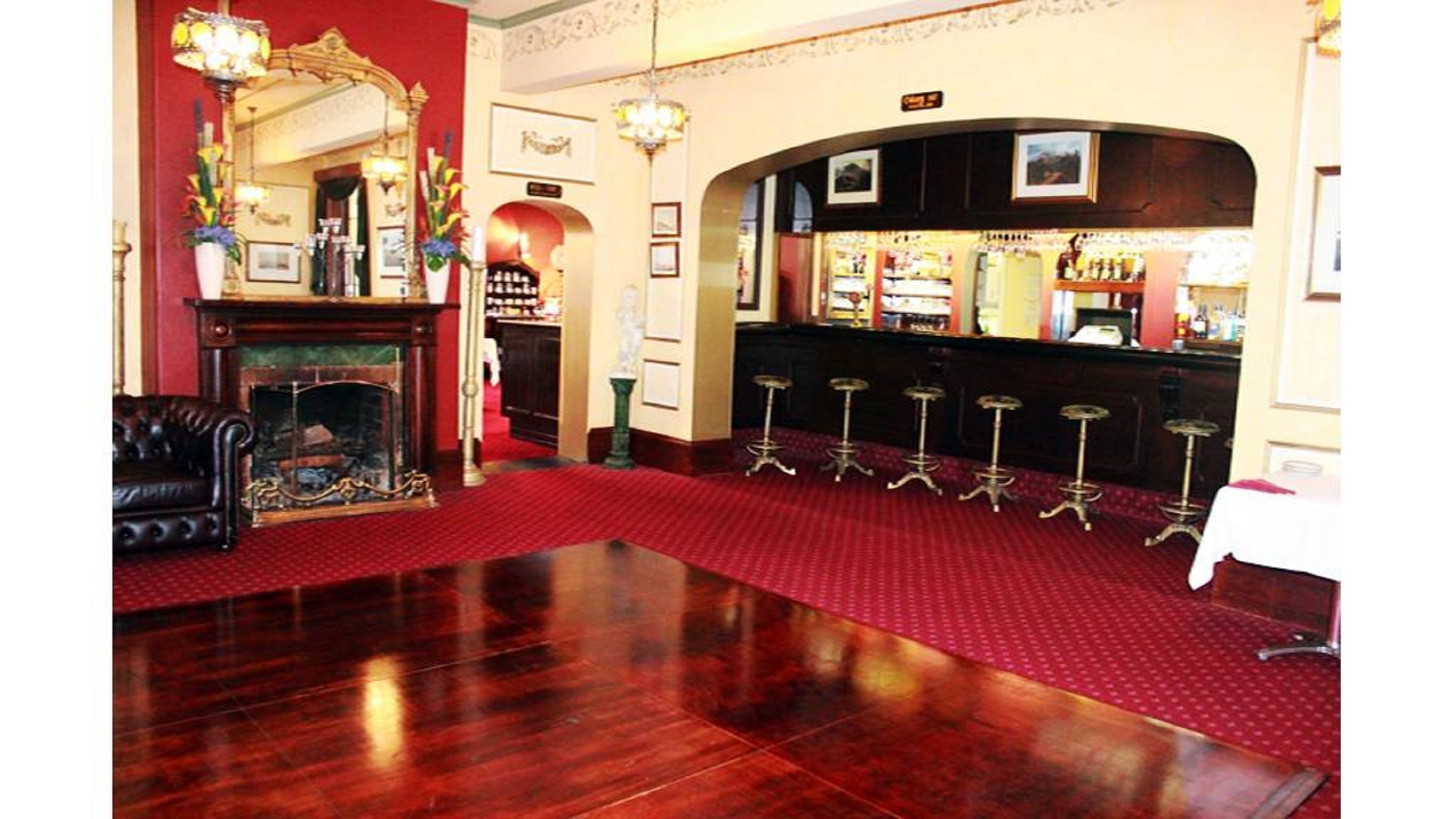 Un hall d’entrée avec un tapis rouge, une cheminée, un coin bar avec des tabourets et un miroir doté d’un cadre décoratif.