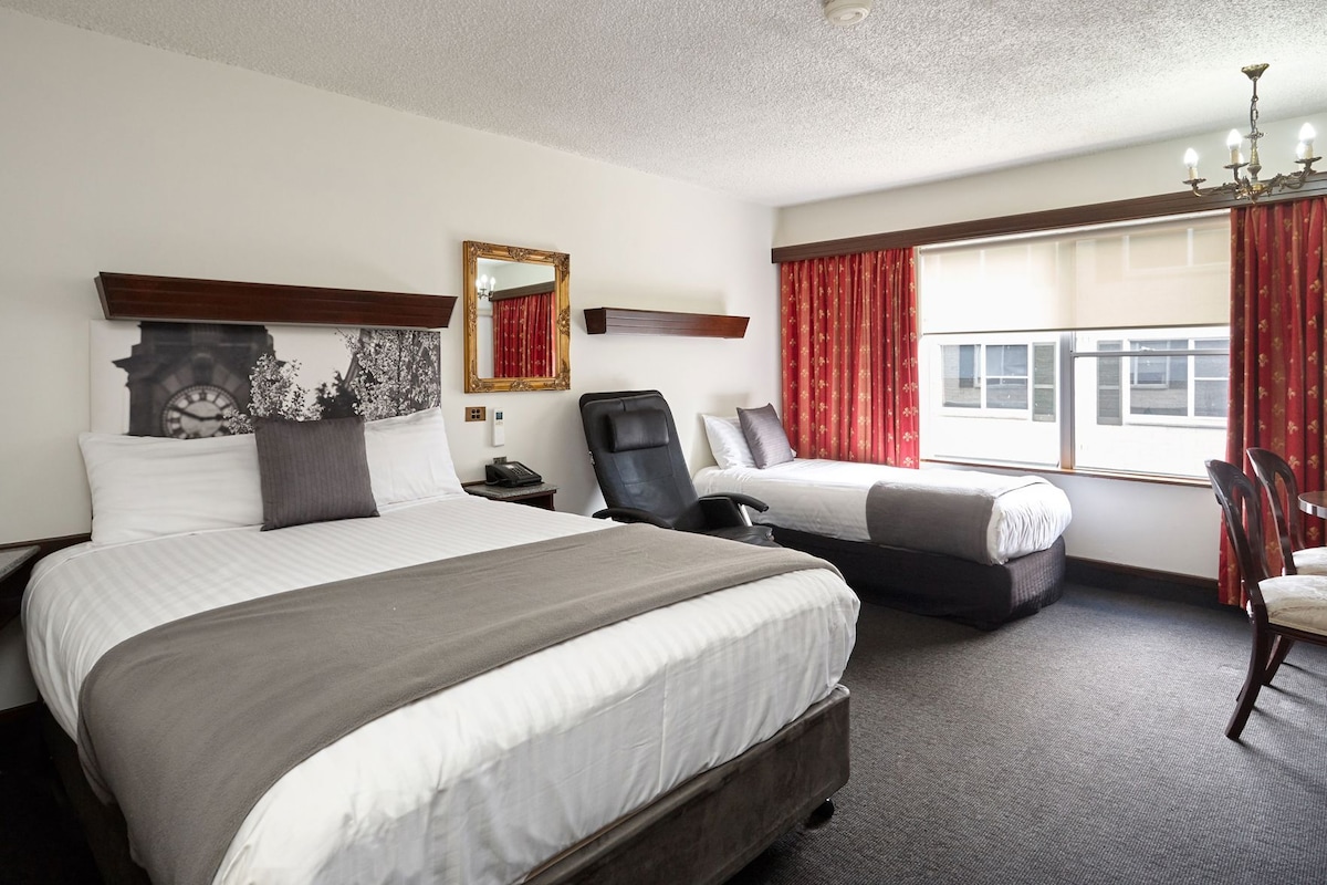 Habitación de hotel con dos camas, un escritorio, una silla, un espejo y una ventana con cortinas.