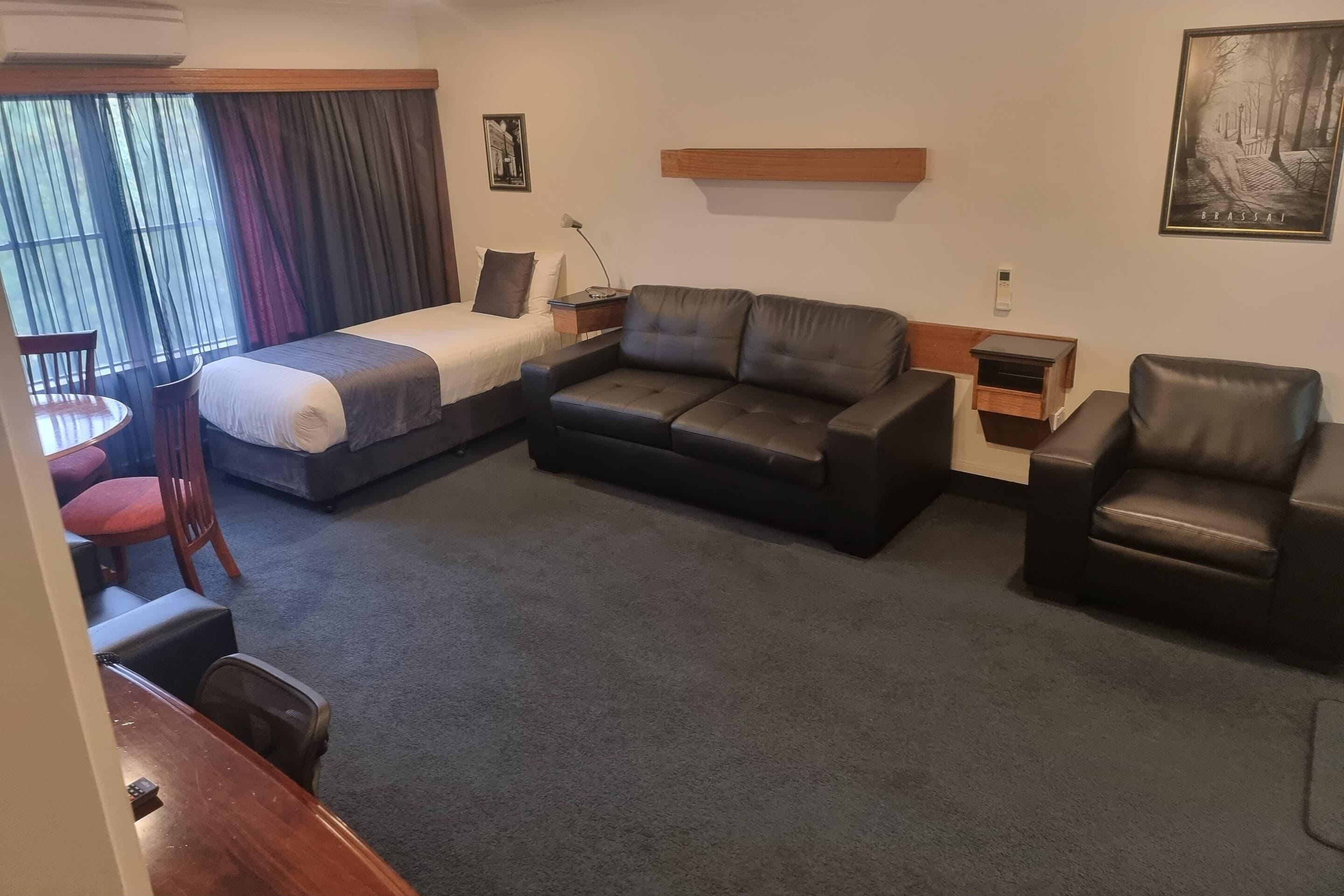 Une chambre d’hôtel avec un lit, un canapé, une chaise, une petite table et une fenêtre avec des rideaux.