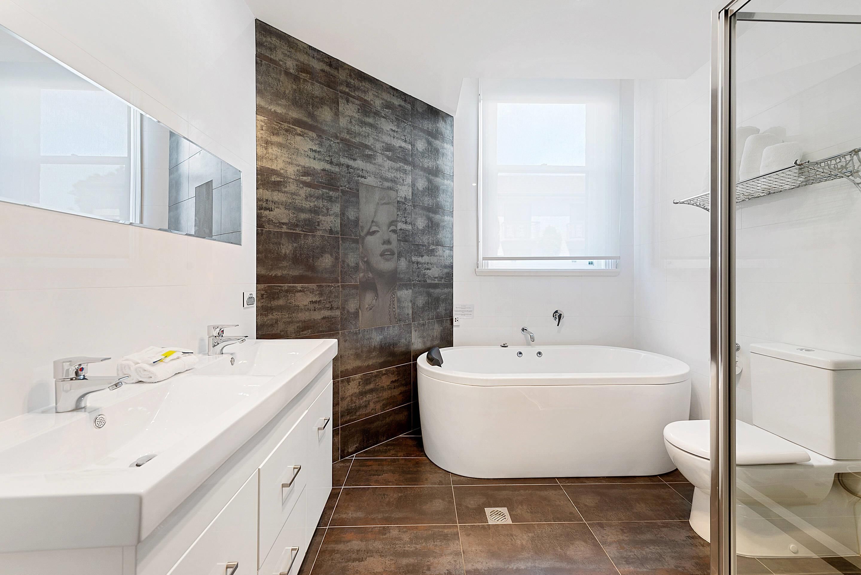 A modern bathroom with a large bathtub, a separate toilet, a vanity with a mirror, and a window providing natural light.