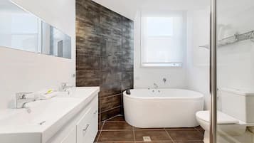 A modern bathroom with a large bathtub, a separate toilet, a vanity with a mirror, and a window providing natural light.