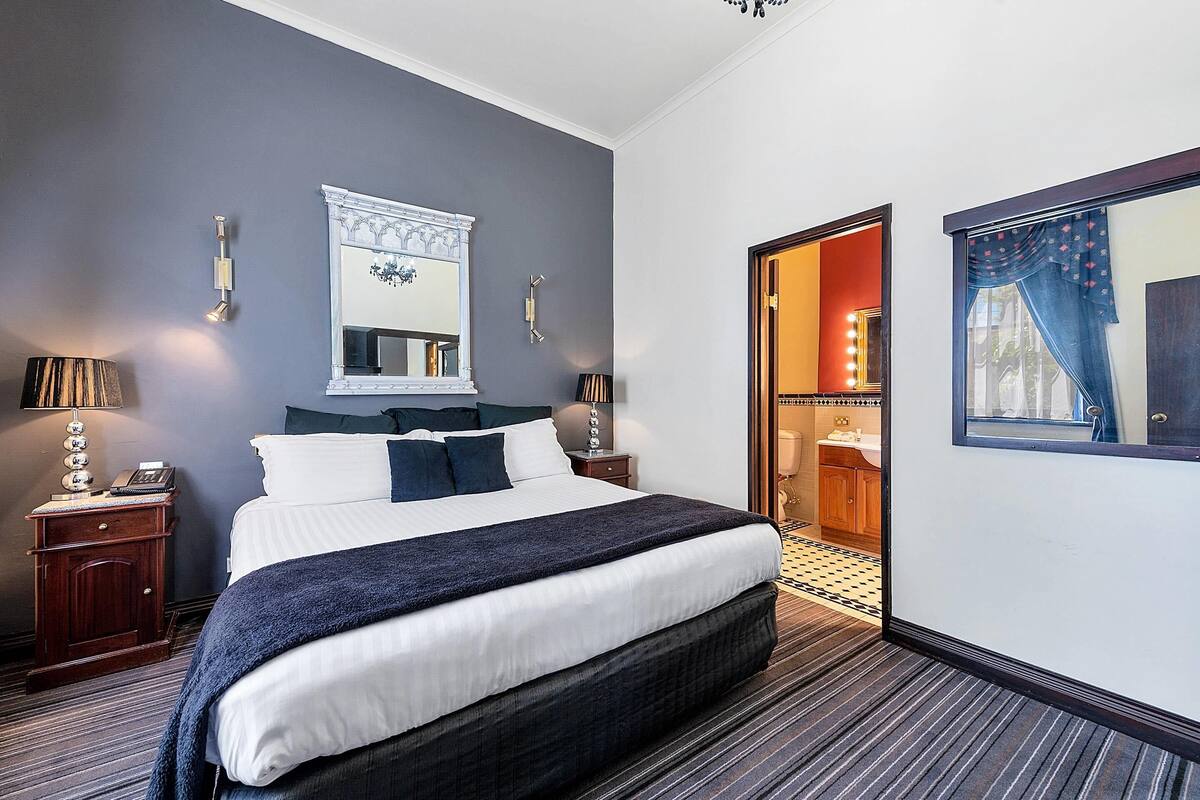 A hotel room with a large bed, bedside lamps, a mirror, and a door leading to a bathroom.