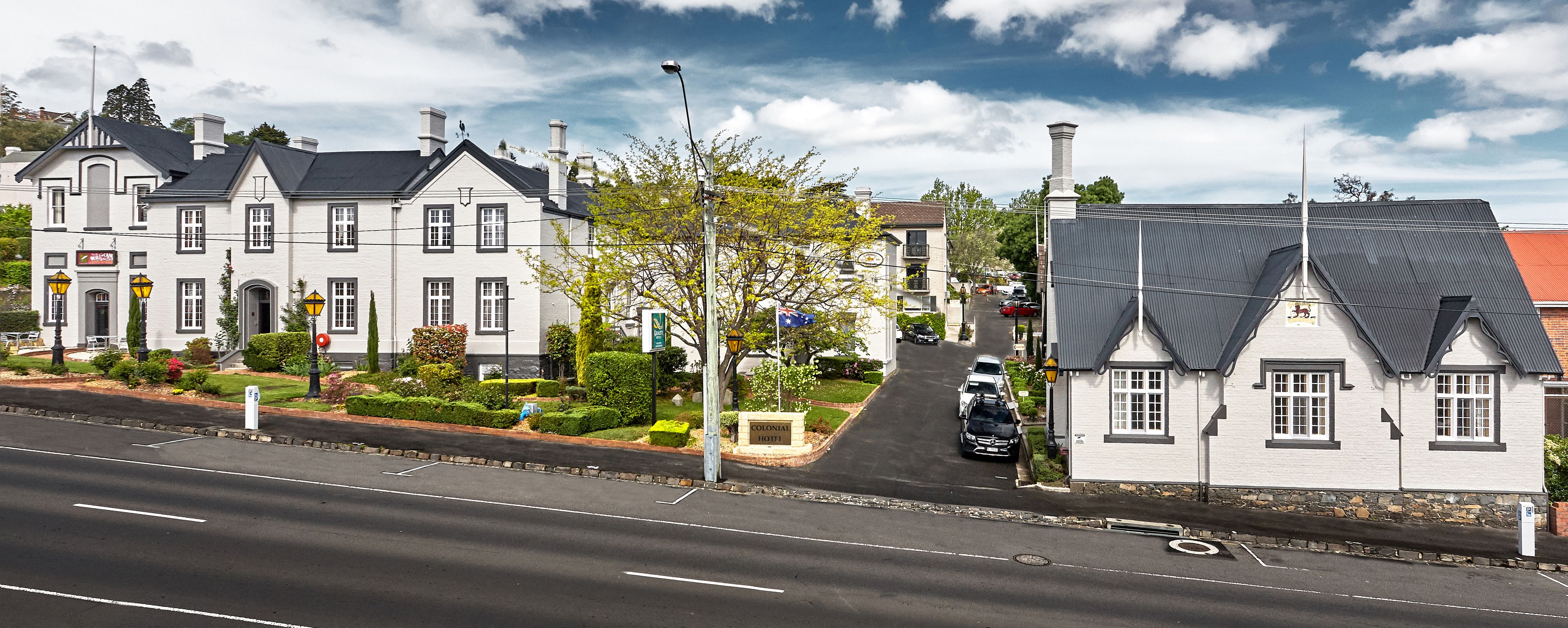 A colonial-style building with a white facade and dark roof, situated on a street with parked cars.