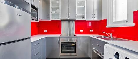 Una cocina compacta con electrodomésticos de acero inoxidable, horno integrado y lavadora.