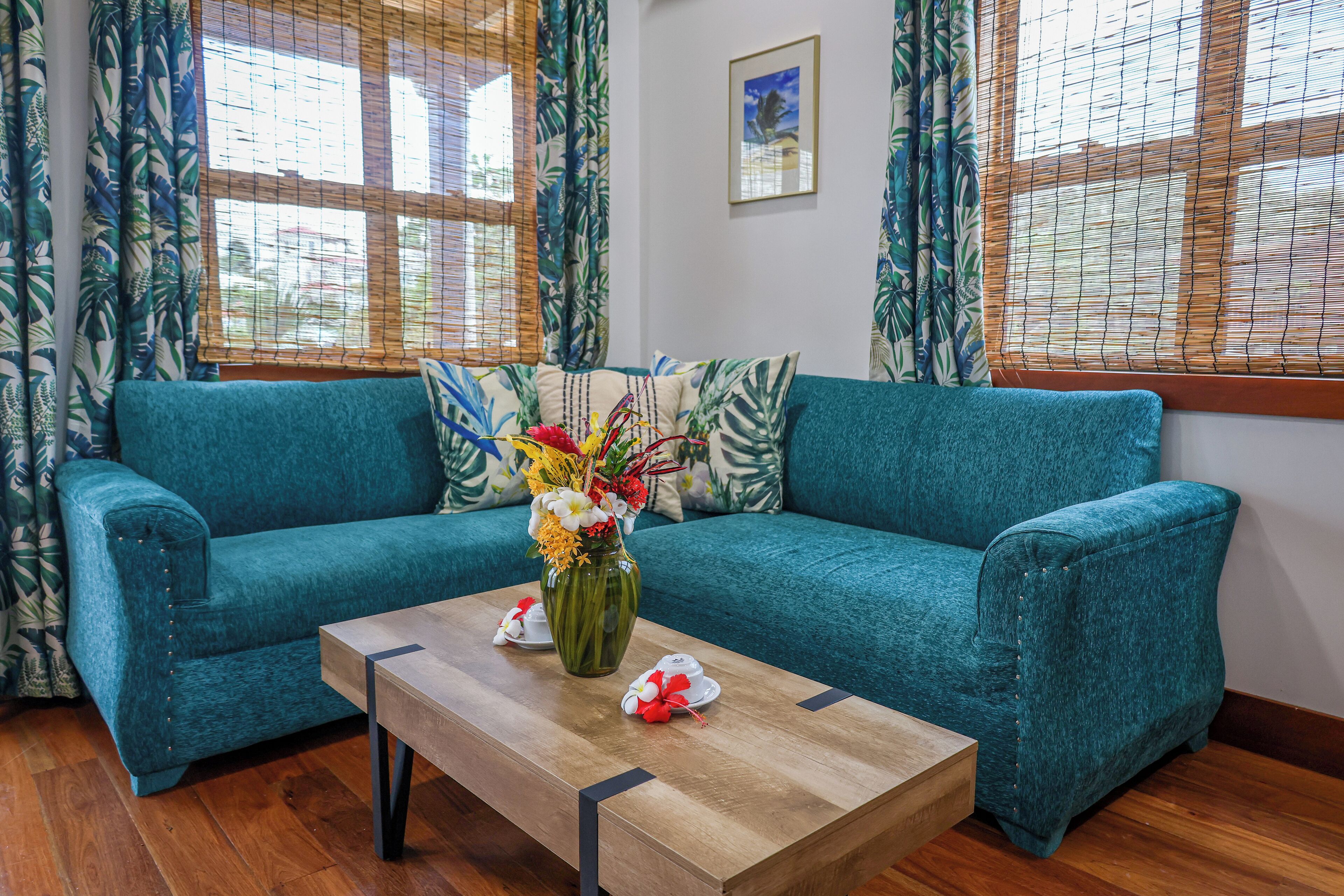 A teal sofa with a wooden coffee table in front, a vase with flowers, and patterned curtains.