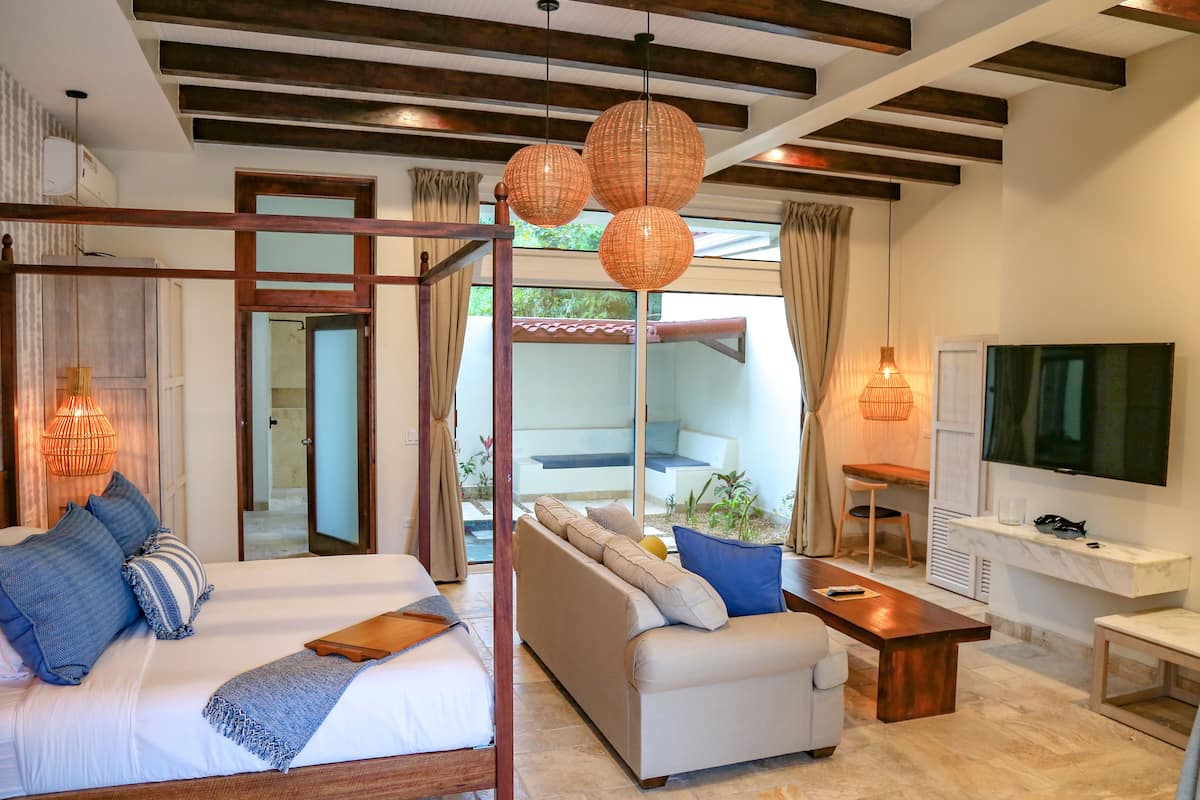 A modern hotel room with a bed, sofa, TV, and a balcony with plants.