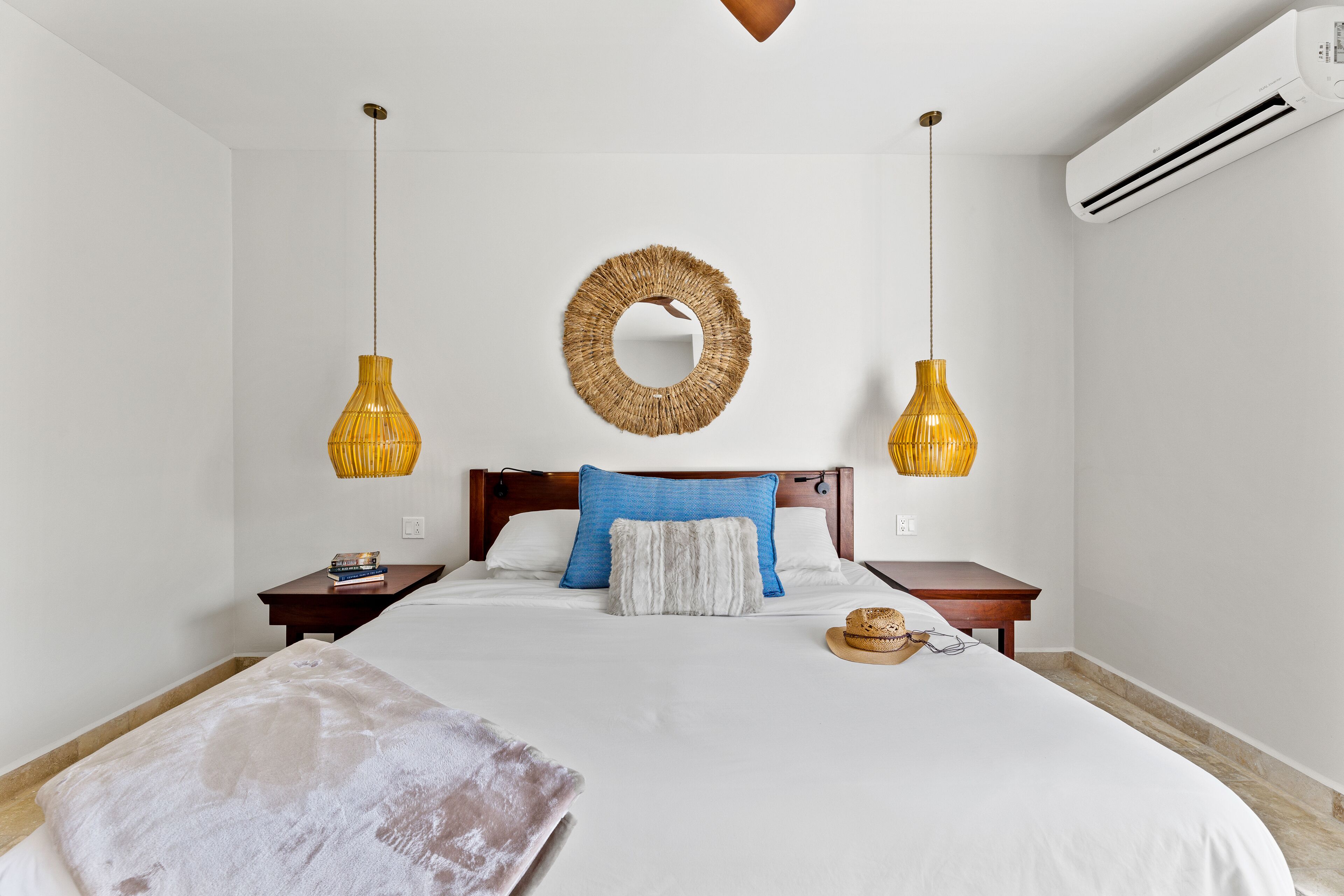 Un dormitorio ordenado con una cama grande, dos mesitas de noche, un espejo en la pared y dos lámparas colgantes.