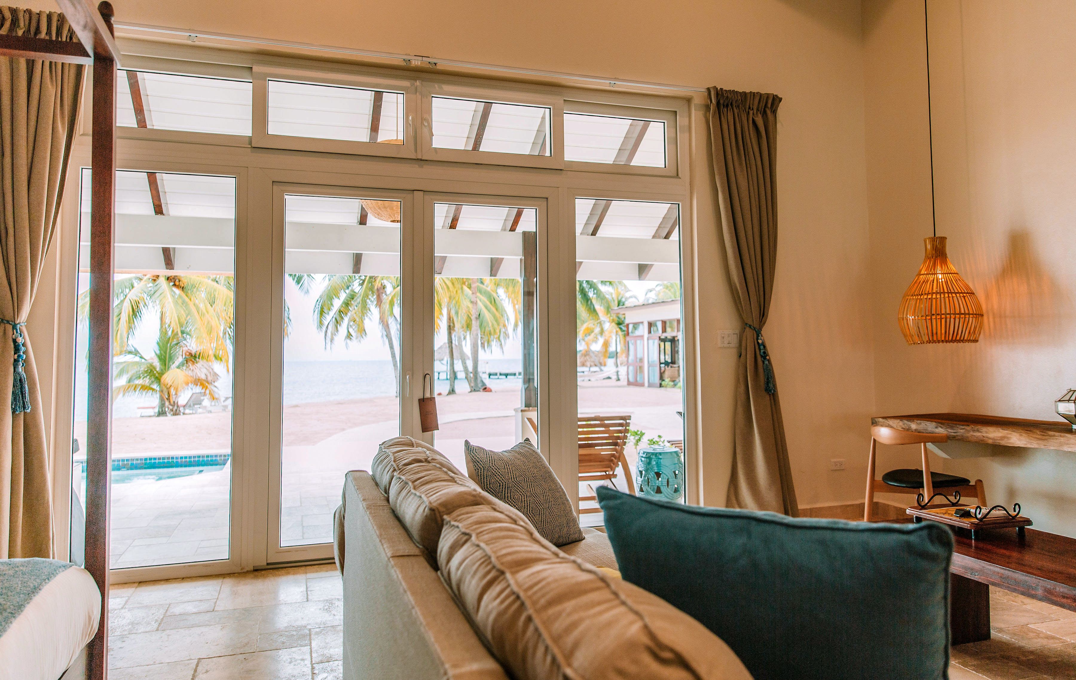 A room with a large sliding glass door leading to a pool area, a sofa with cushions, a small table, and a hanging light fixture.
