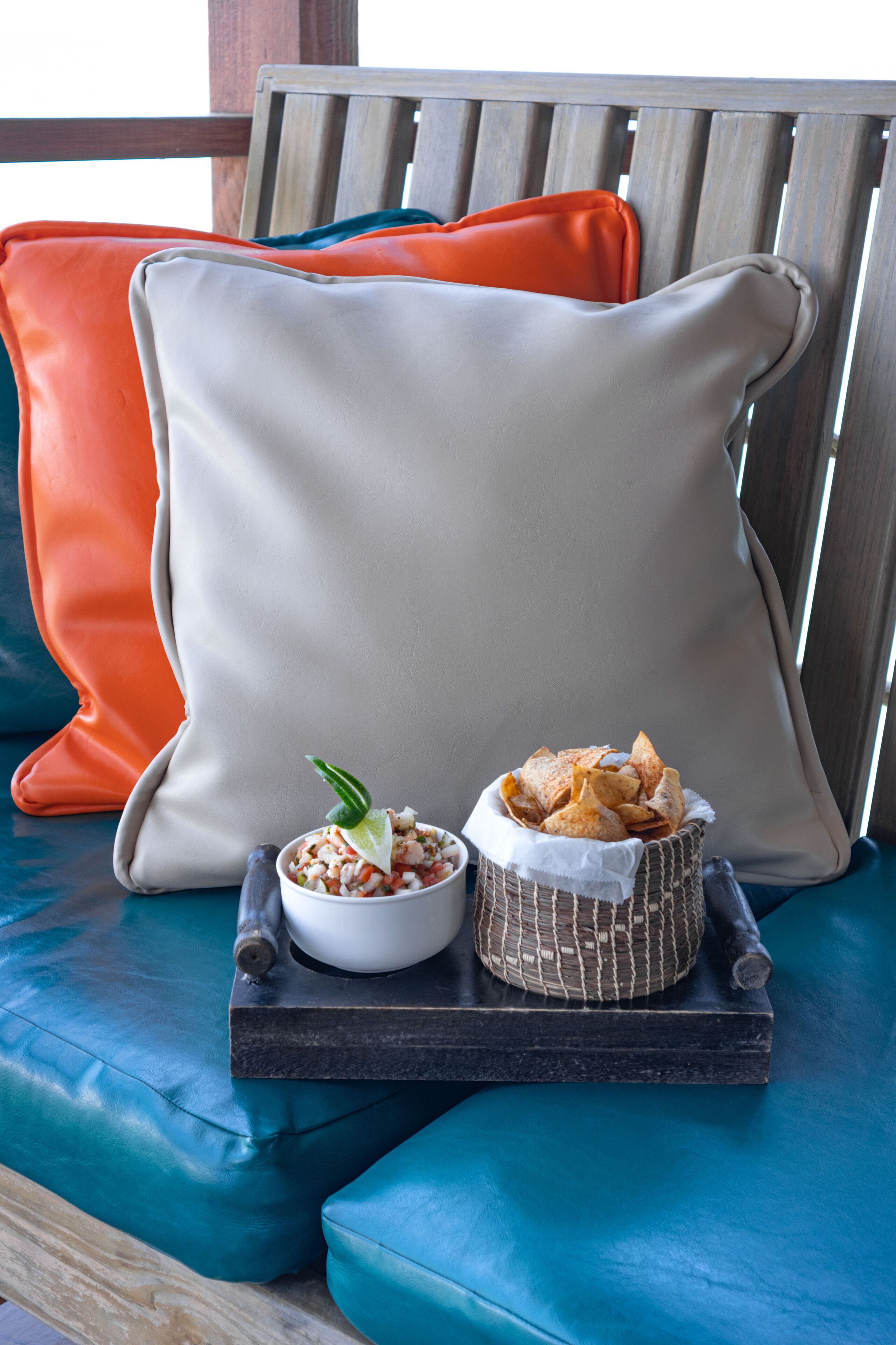Una zona de estar con cojines color turquesa, un almohadón blanco y una bandeja con aperitivos y un tazón de comida.