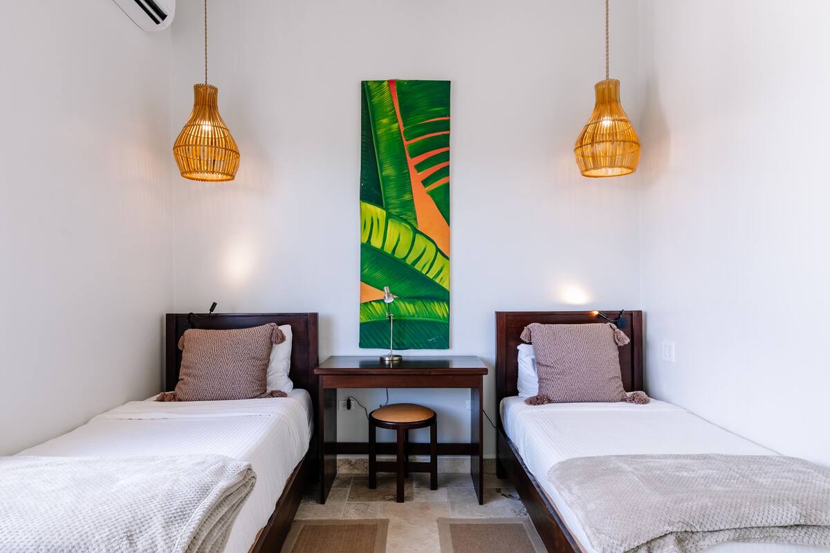 A bedroom with two single beds, a desk, and two pendant lights.