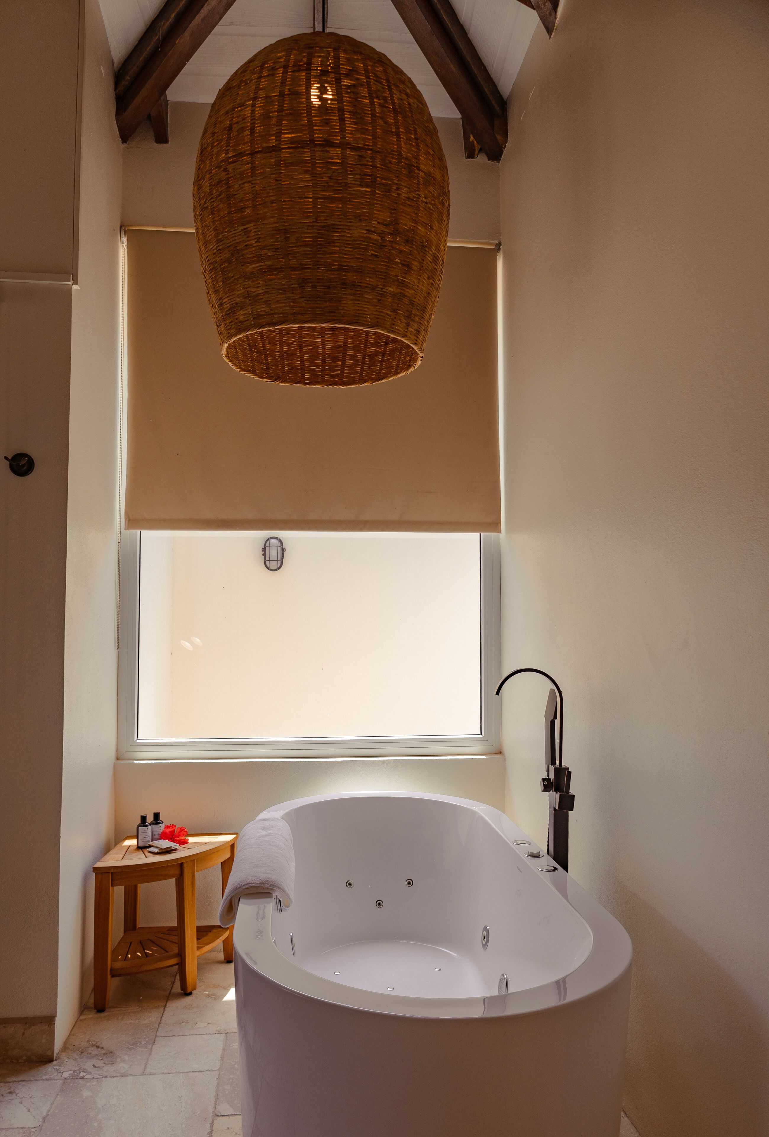 Une salle de bain moderne avec une baignoire sur pieds, une grande fenêtre et un luminaire suspendu en osier.