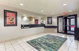 Un vestíbulo de hotel con un mostrador de recepción, obras de arte enmarcadas, una alfombra estampada y una entrada con puerta de cristal.