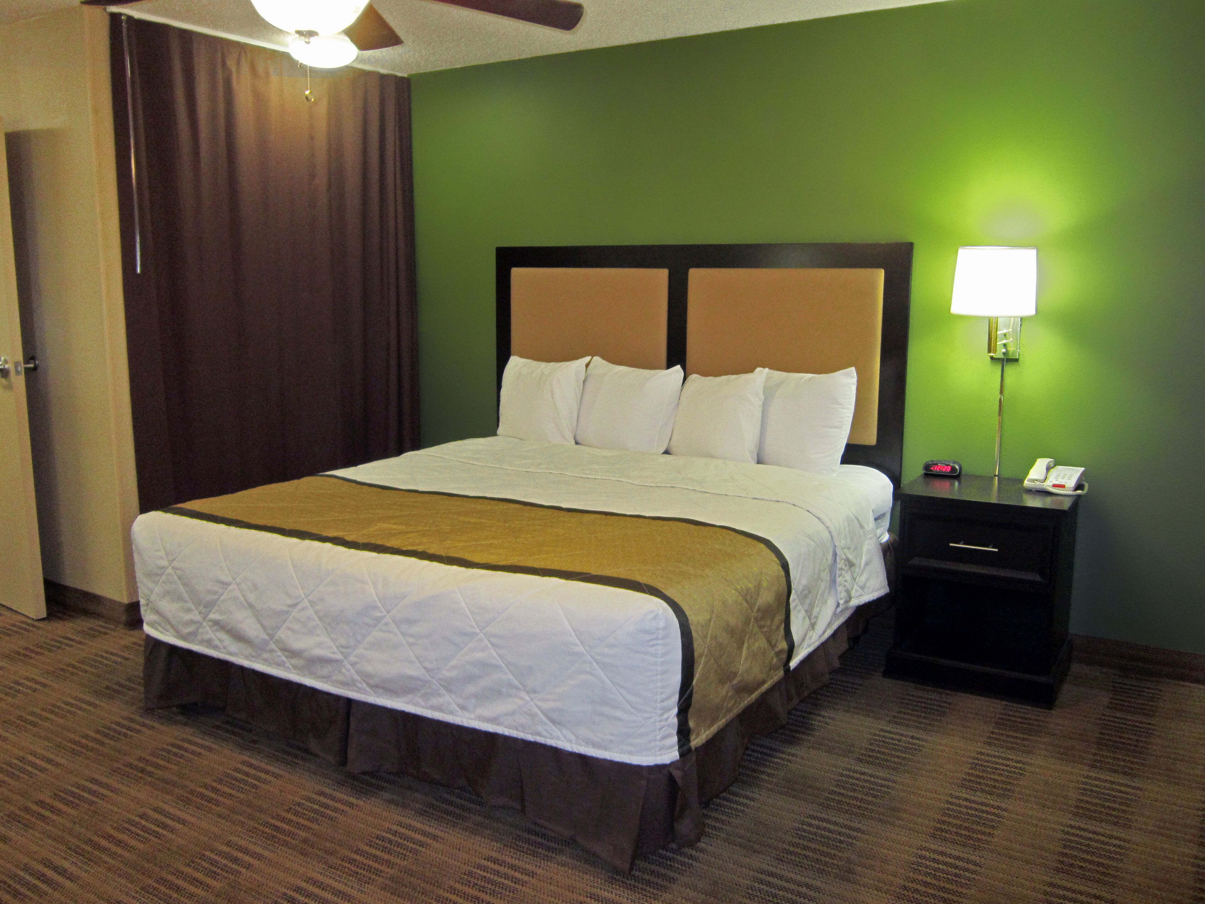 A hotel room with a large bed, a nightstand with a lamp, and a green wall.