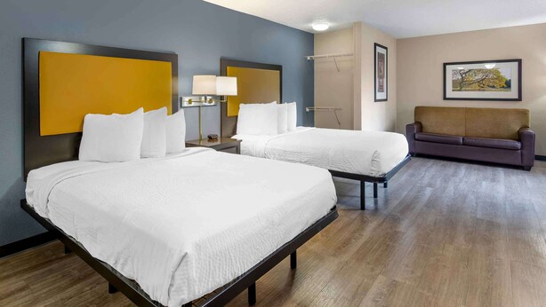 A hotel room with two beds, a sofa, a nightstand with a lamp, and a framed picture on the wall. - Extended Stay America Suites Memphis Germantown West (Memphis)