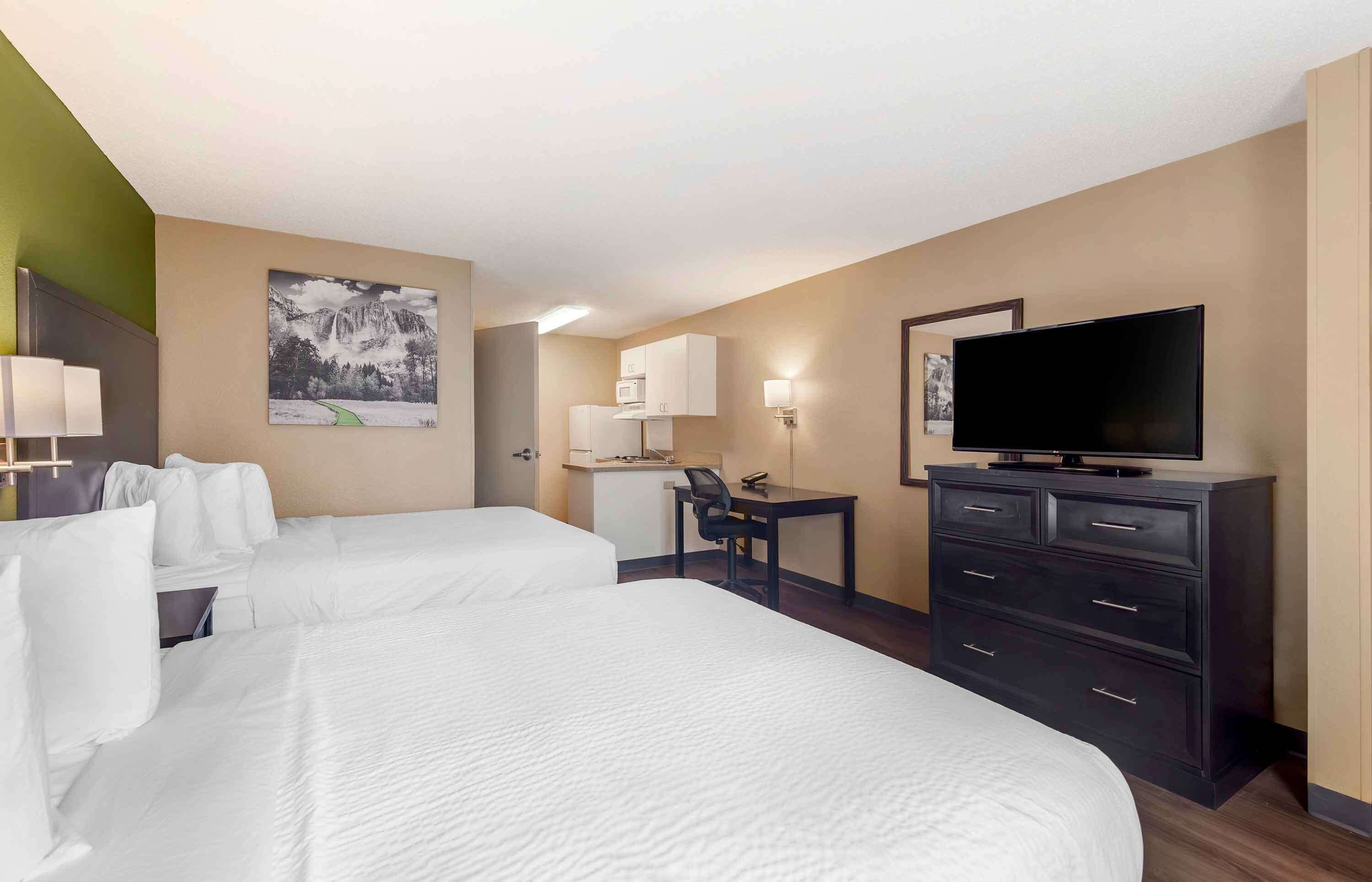 A hotel room with two beds, a desk, a television, and a painting on the wall.