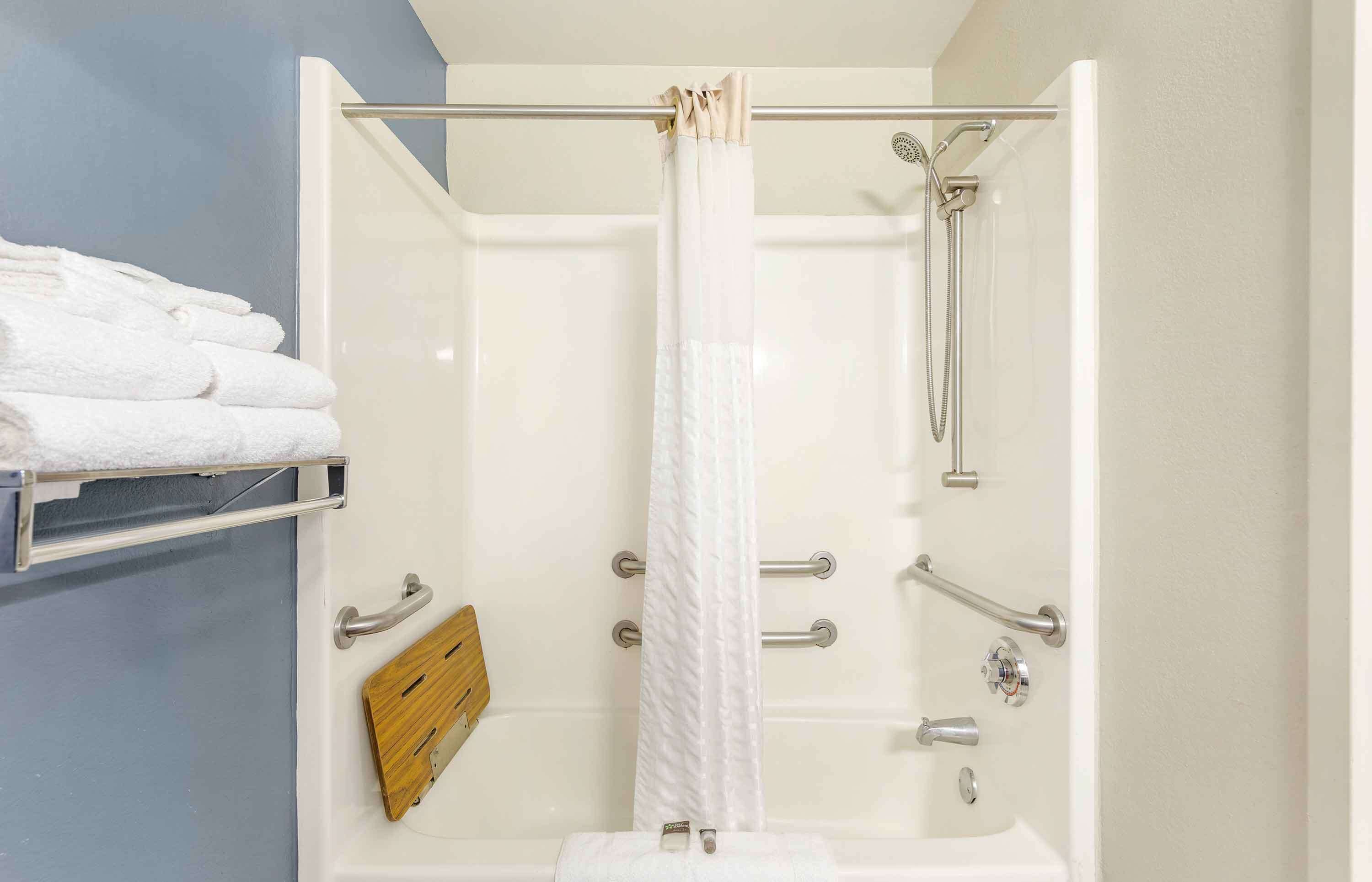 A shower with a glass door, a towel rack with folded towels, a wooden shelf, and a handheld showerhead.
