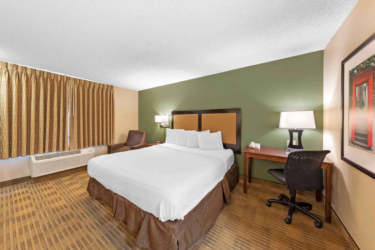 A hotel room with a large bed, a desk with a chair, a lamp, and a framed picture on the wall.