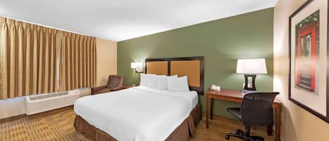 A hotel room with a large bed, a desk with a chair, a lamp, and a framed picture on the wall.