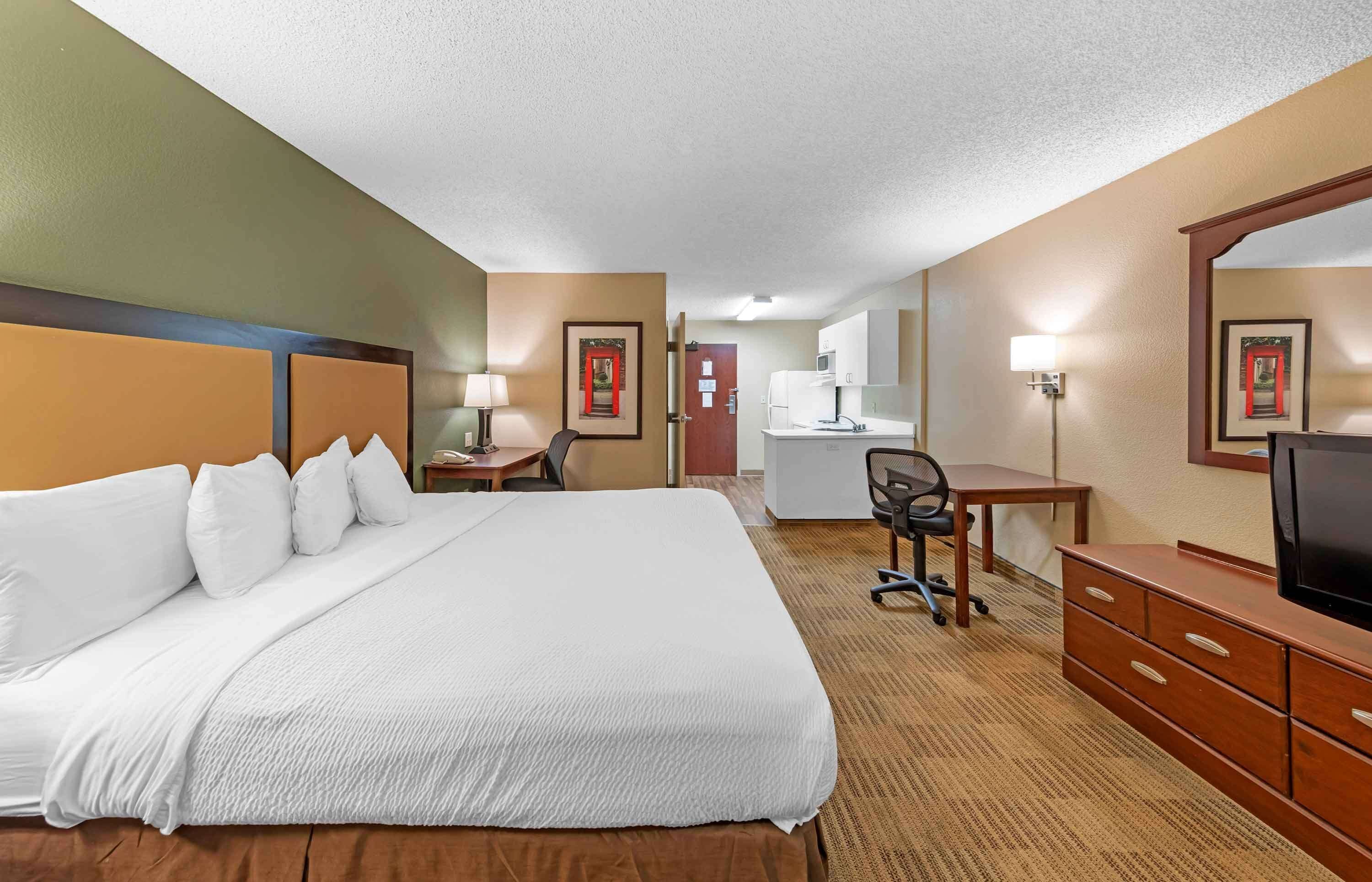 Een hotelkamer met een groot bed, een bureau, een stoel, een televisie en een kitchenette.