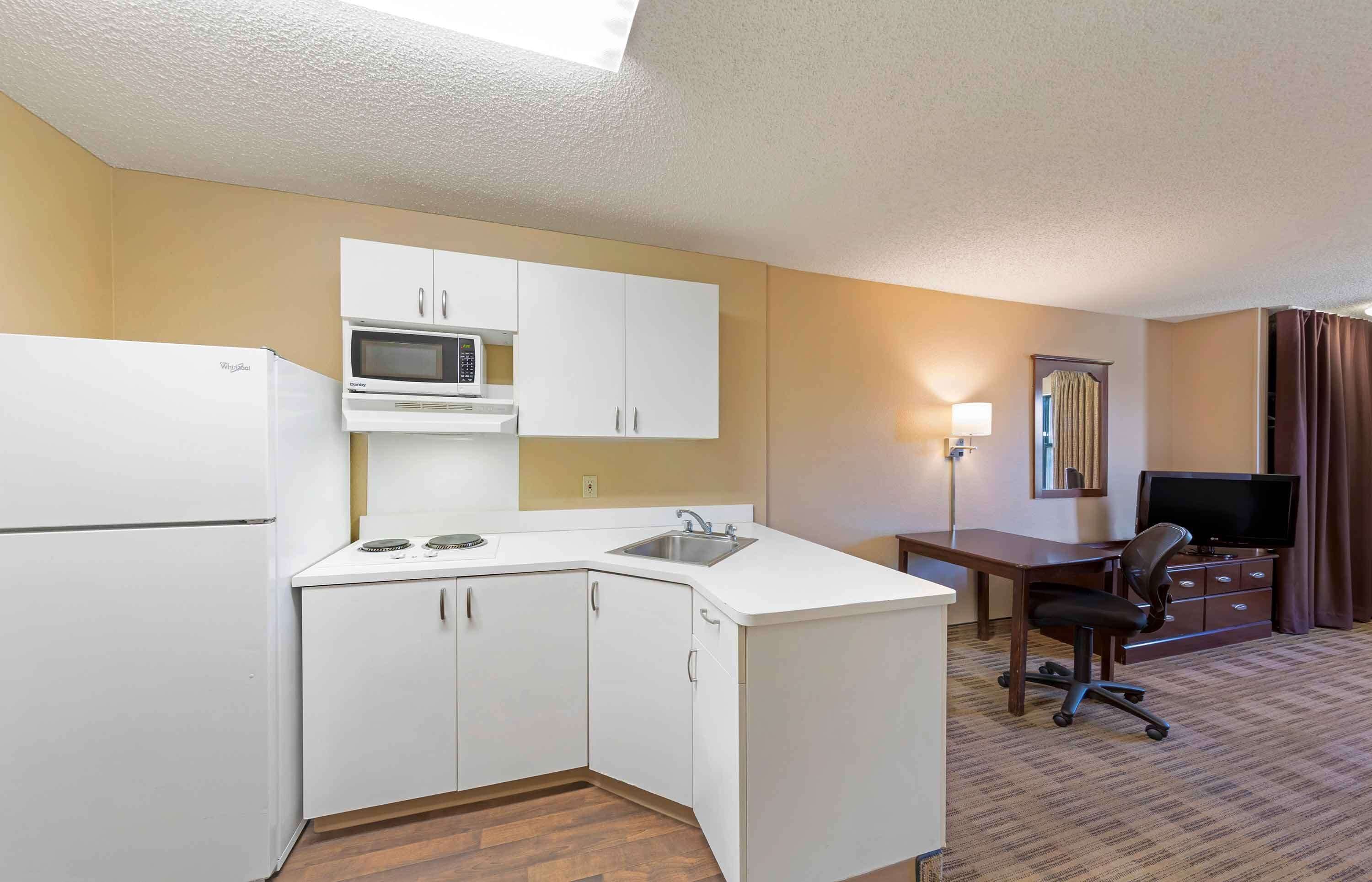 A compact hotel room with a kitchenette, a desk, a chair, and a television.