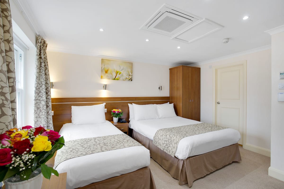 Habitació d'hotel amb dos llits, una taula de nit, un armari de fusta, un quadre a la paret i un vas de flors.