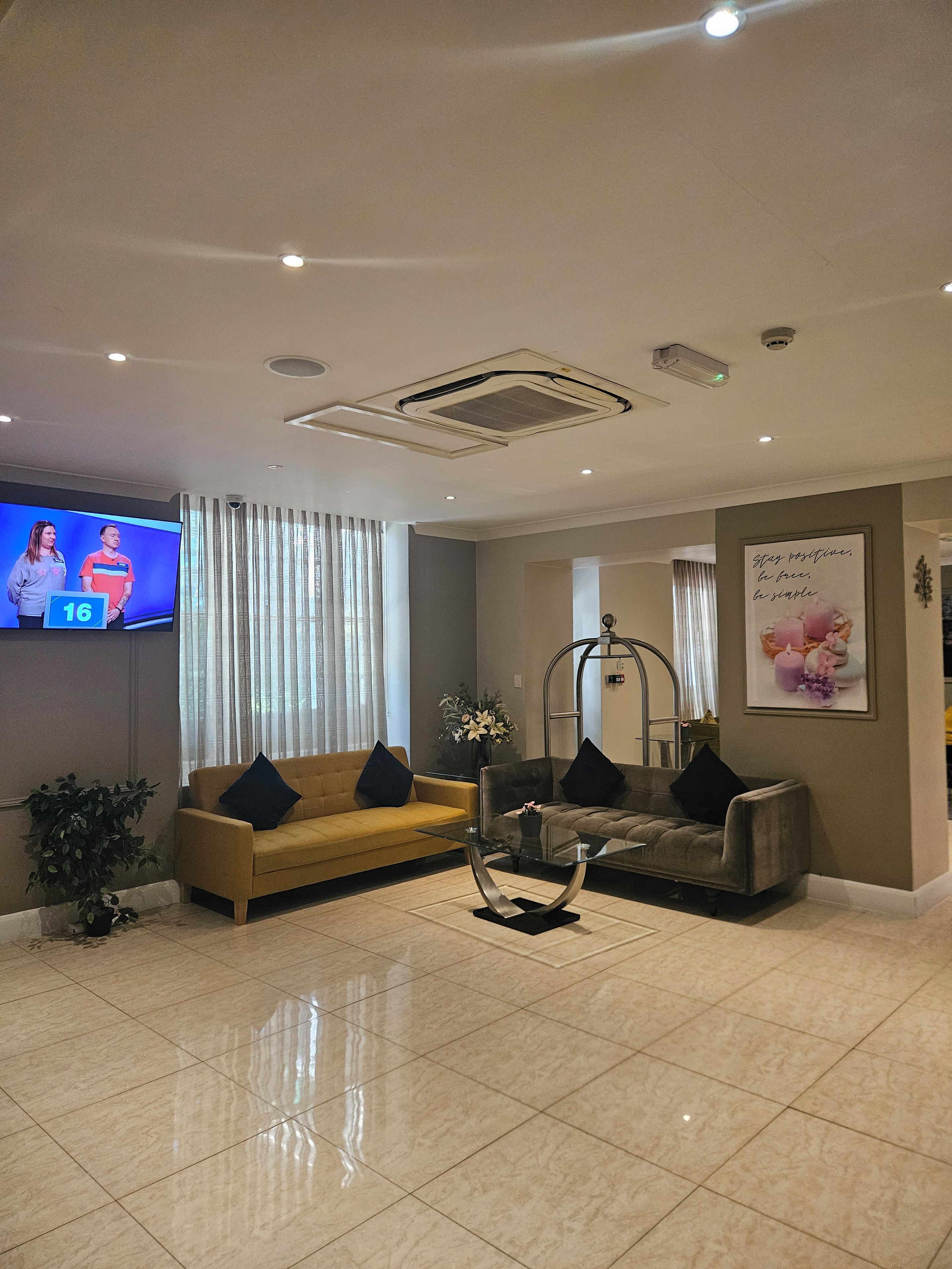 Un moderno vestíbulo de hotel con una televisión de pantalla plana, dos sofás, una mesa de centro de vidrio y una pieza decorativa en la pared.