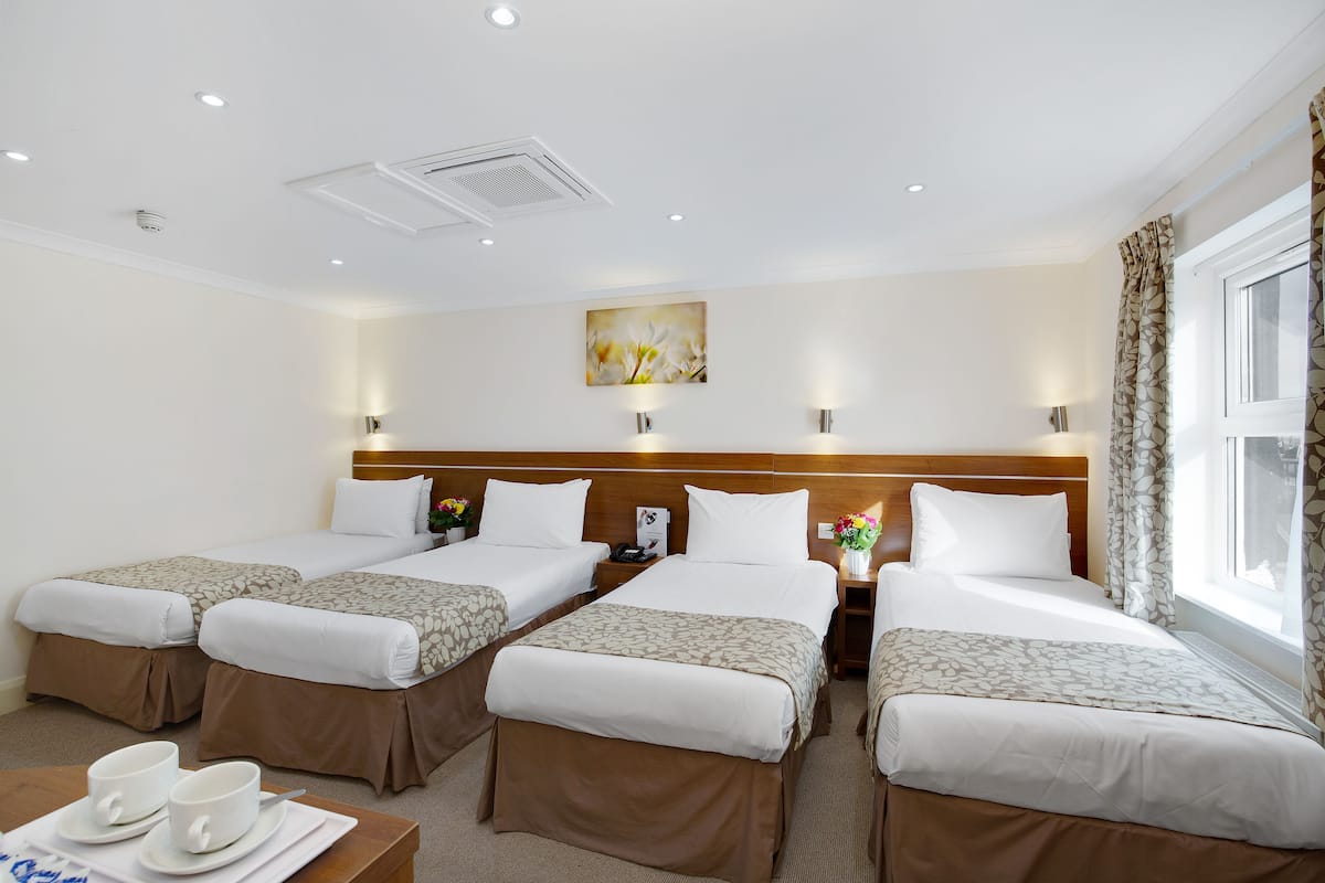 Habitació d'hotel amb quatre llits, una taula de menjador amb tasses i platets, i un quadre a la paret.