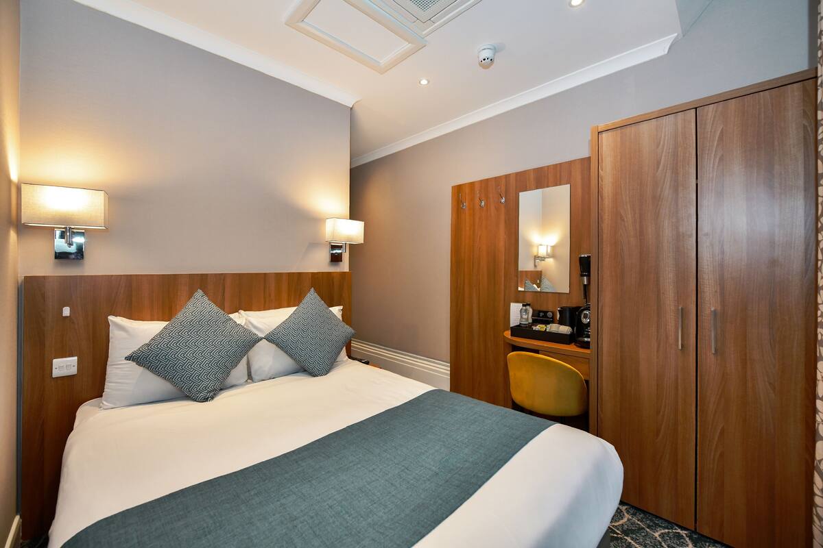 Habitació d'hotel amb un llit gran, un armari de fusta i una taula de treball amb una cadira.