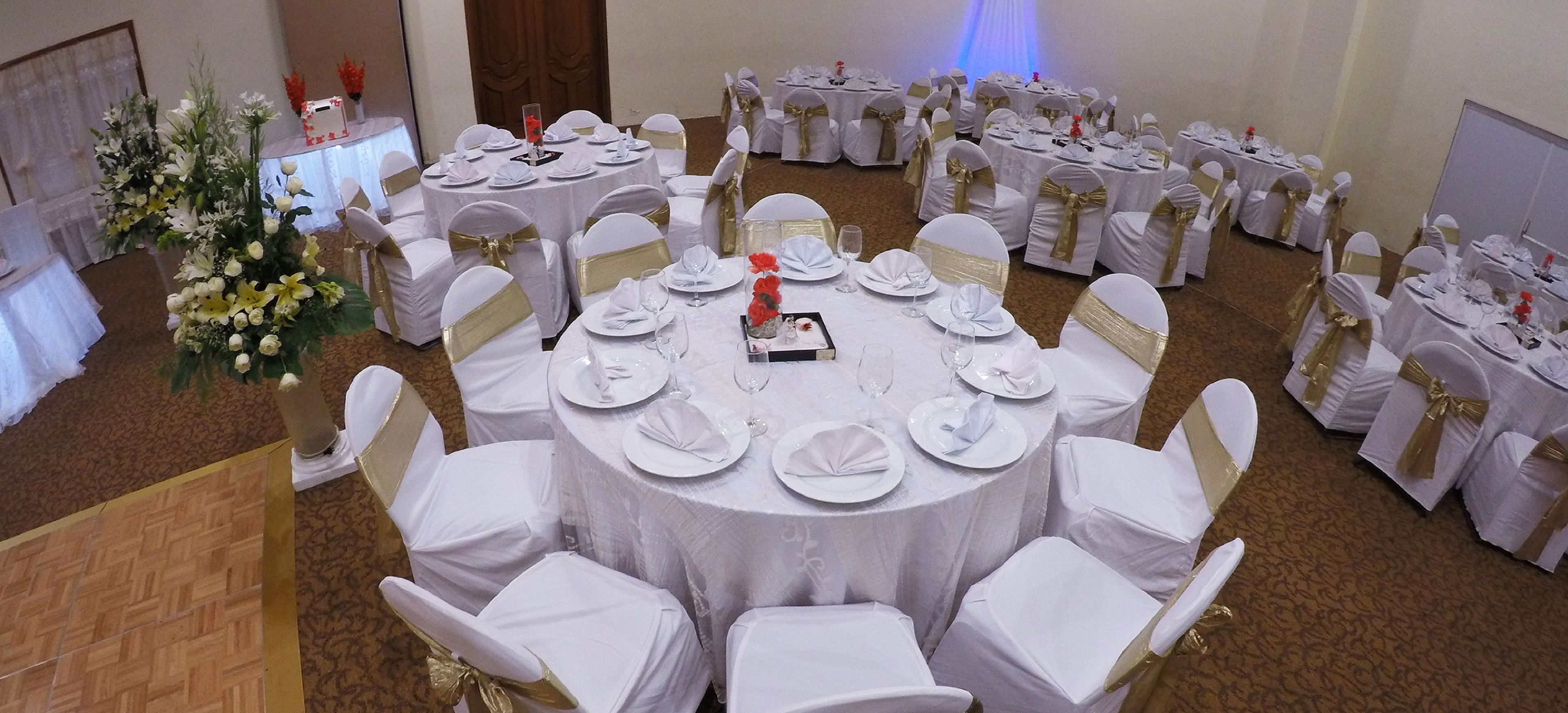 A banquet hall with round tables set for a formal event, each with white tablecloths and gold sashes.