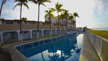 Una piscina con agua cristalina que refleja palmeras y un edificio con varios balcones.