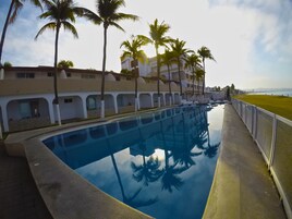 Una piscina con agua cristalina que refleja palmeras y un edificio con varios balcones.