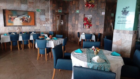 A restaurant interior with stone walls, blue chairs, and tables set with white tablecloths and blue napkins.