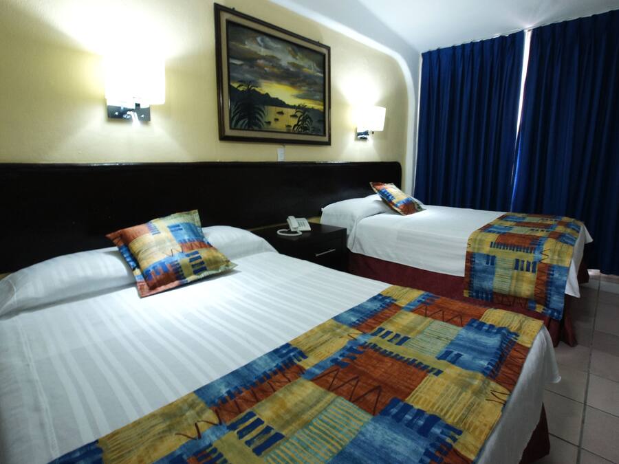 A hotel room with two beds, each with a patterned bedspread, a nightstand with a telephone, and a wall-mounted lamp.