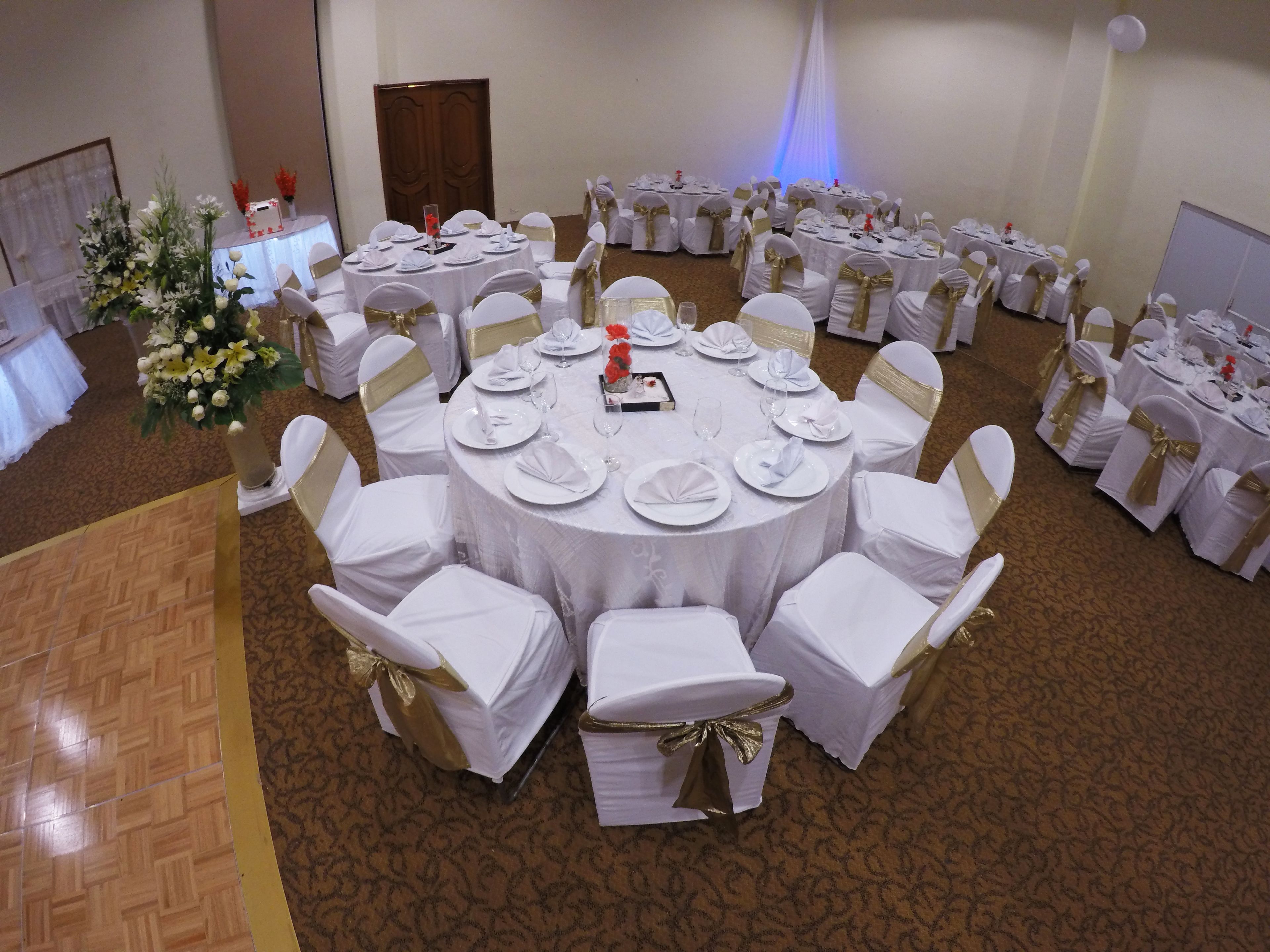 A banquet hall with round tables set for a formal event, featuring white tablecloths and gold sashes.