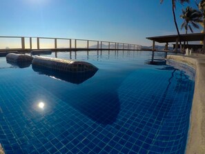 A swimming pool with clear blue water, a bridge in the background, and palm trees. - Hotel Marbella (Manzanillo)
