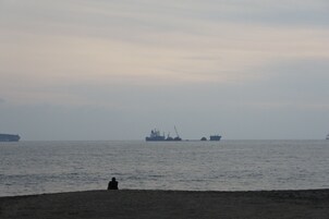 Una playa con una persona sentada en la arena, mirando al mar.