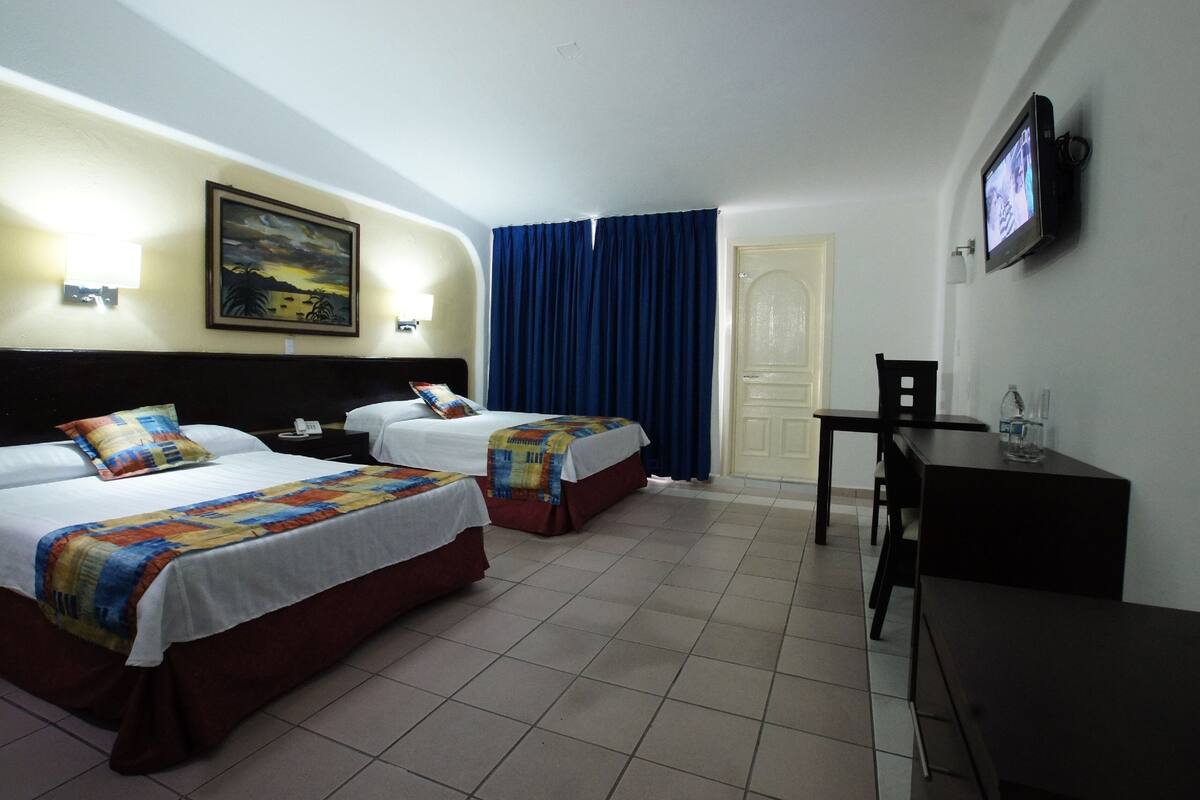A hotel room with two beds, a desk, a chair, a TV, and a painting on the wall.